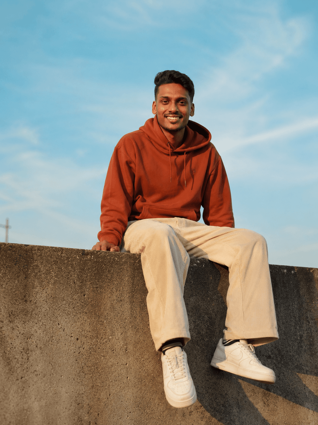 Afthar N N, sitting on a low concrete wall against an open sky